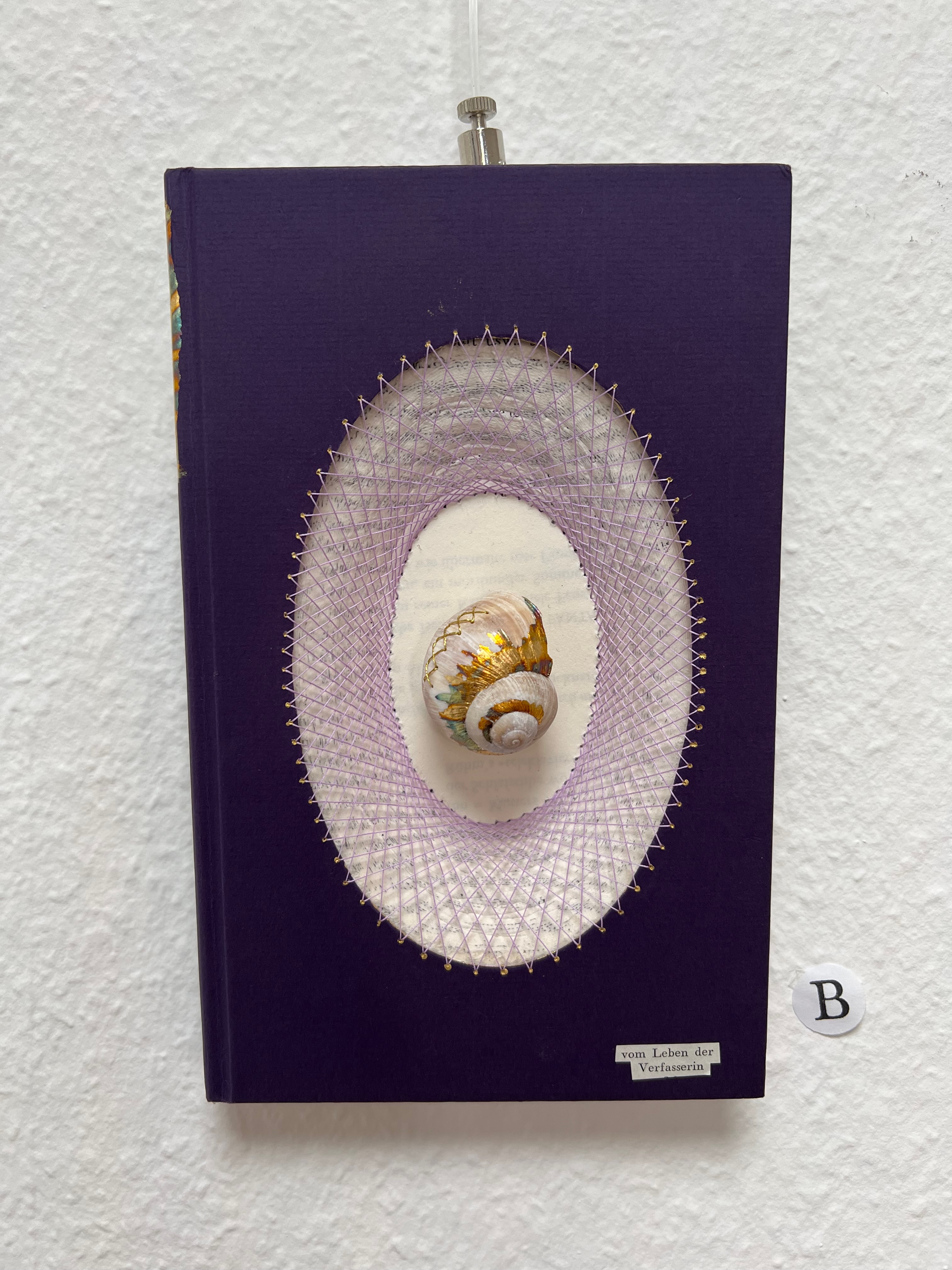 Lila Buch mit Schneckenhaus im Cover und Fadenkunst