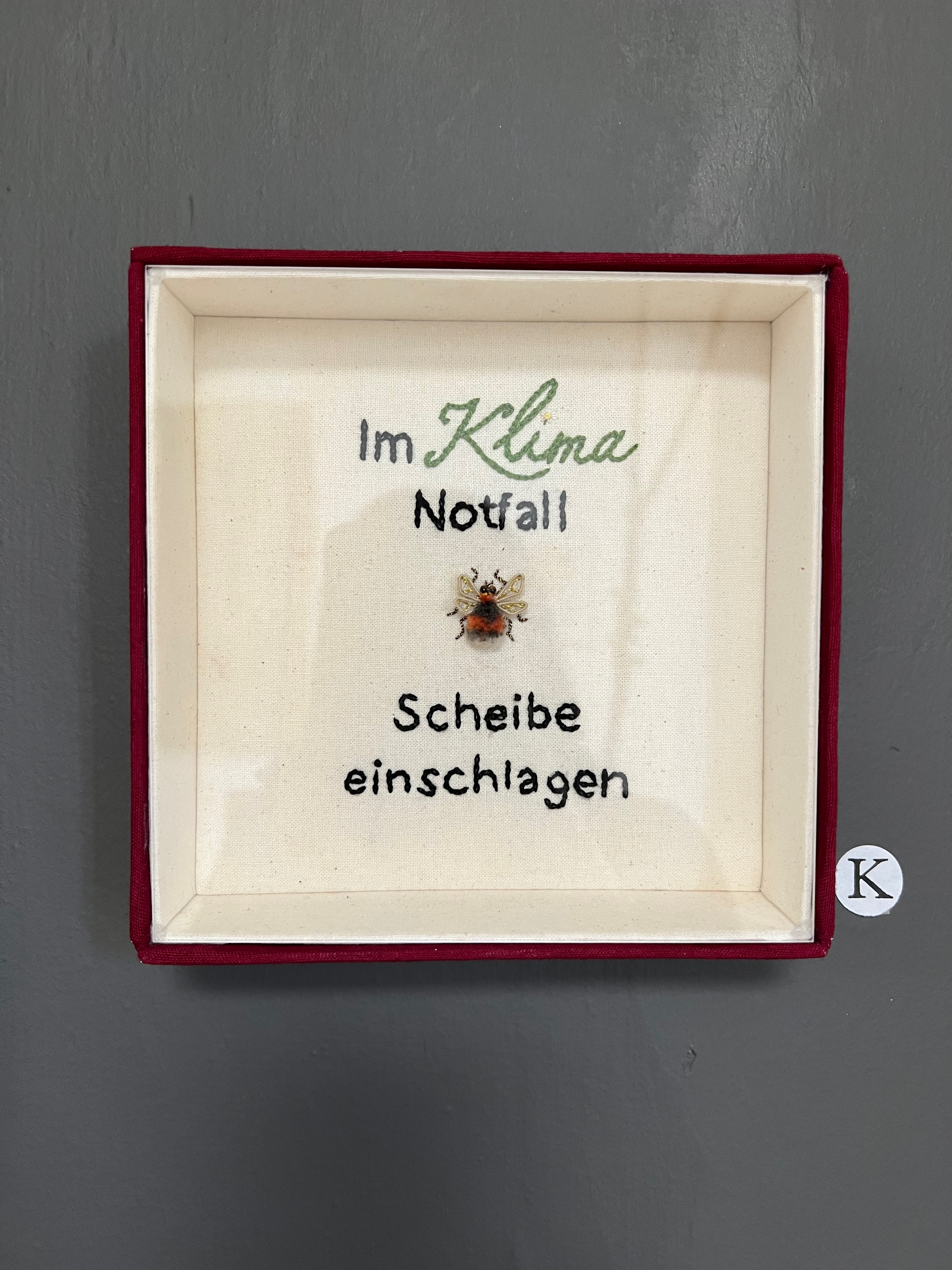 Stickarbeit in Feuermelder-Optik "im Klimanotfall, bitte Scheibe einschlagen"